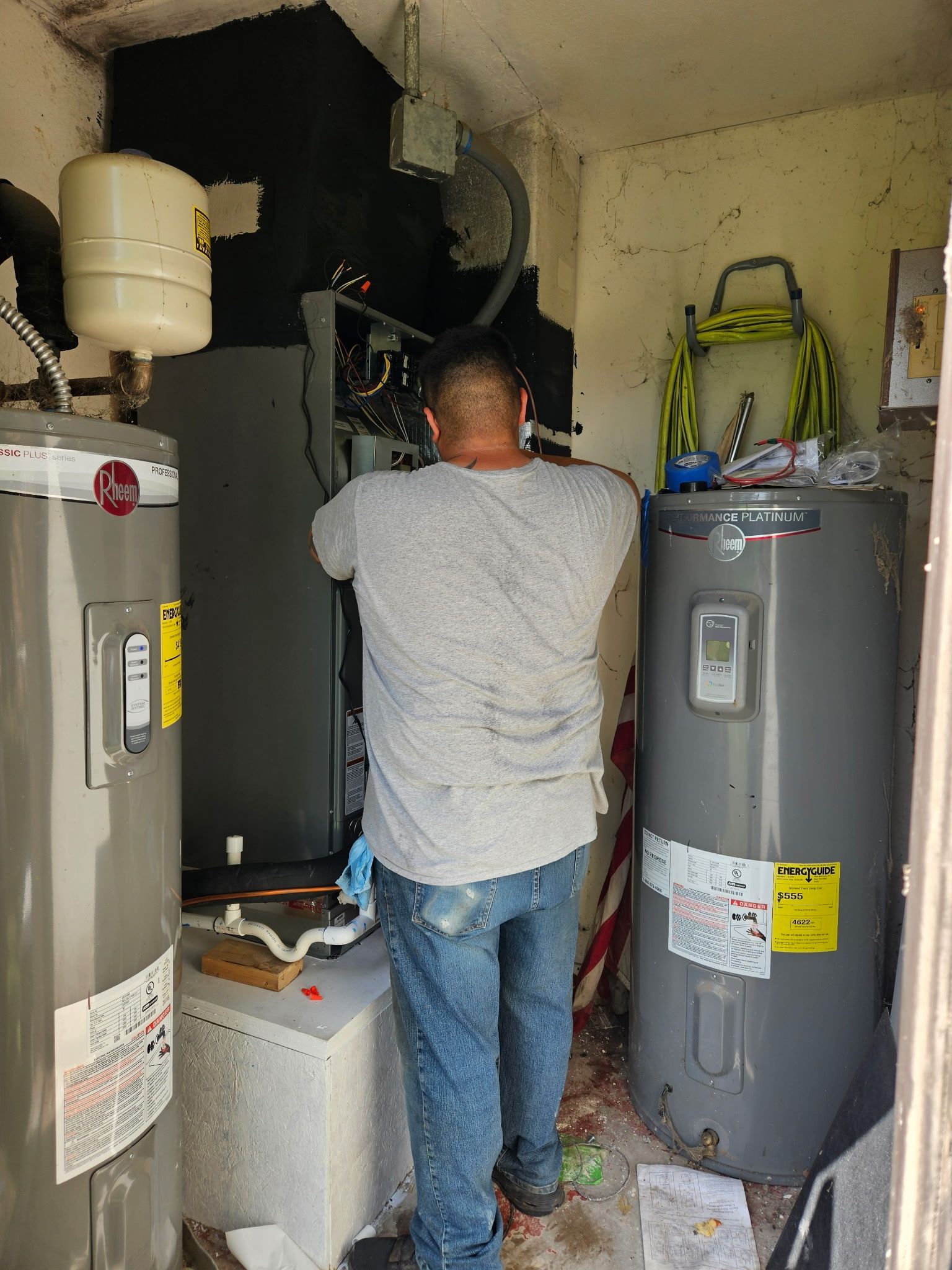 A person working on an HVAC system in a utility room with two water heaters.