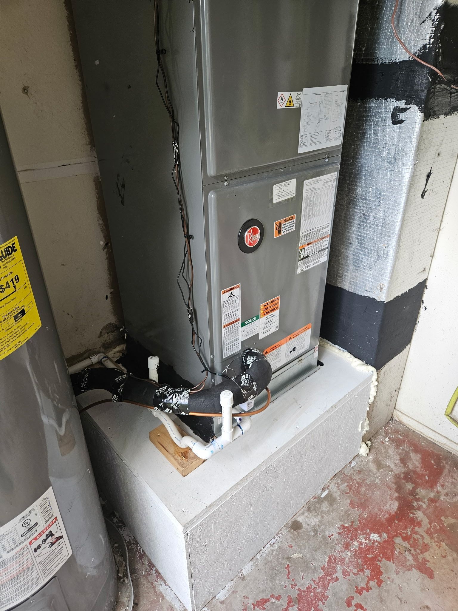 Furnace and water heater in a utility room. Gray metal units, white pipes, and concrete blocks.