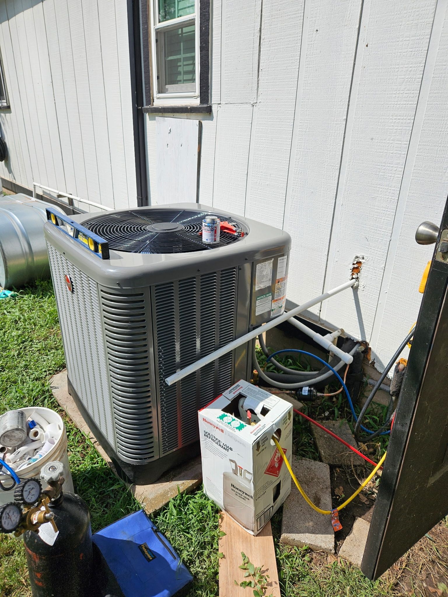 Air conditioner unit being serviced outdoors, with gauges and tools visible.