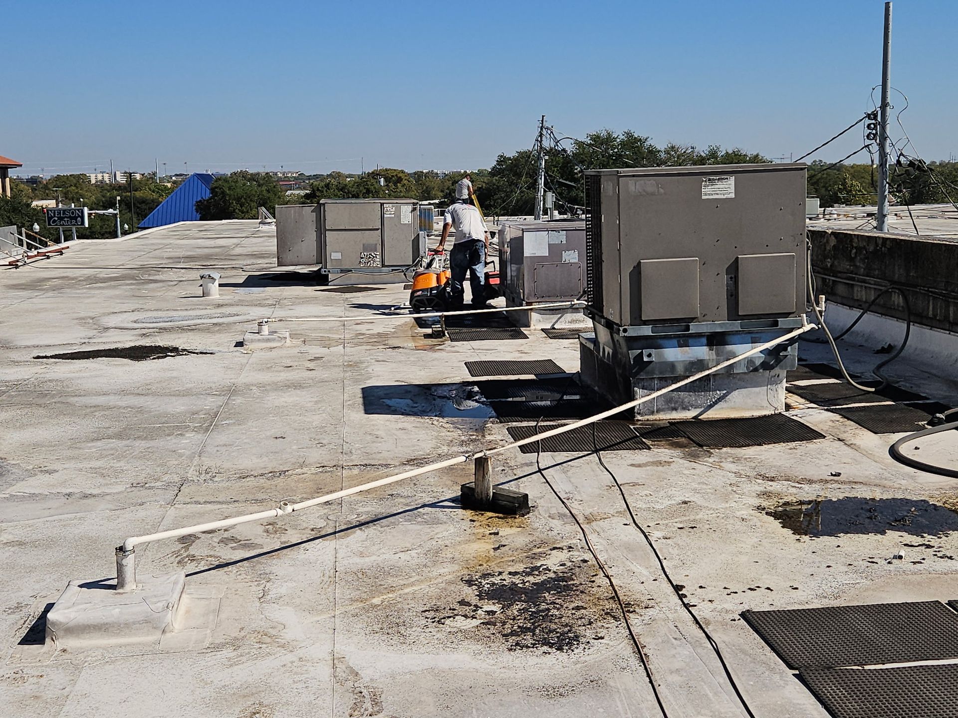 Man on rooftop, repairing HVAC unit. Sunny day, with various units and safety railing.