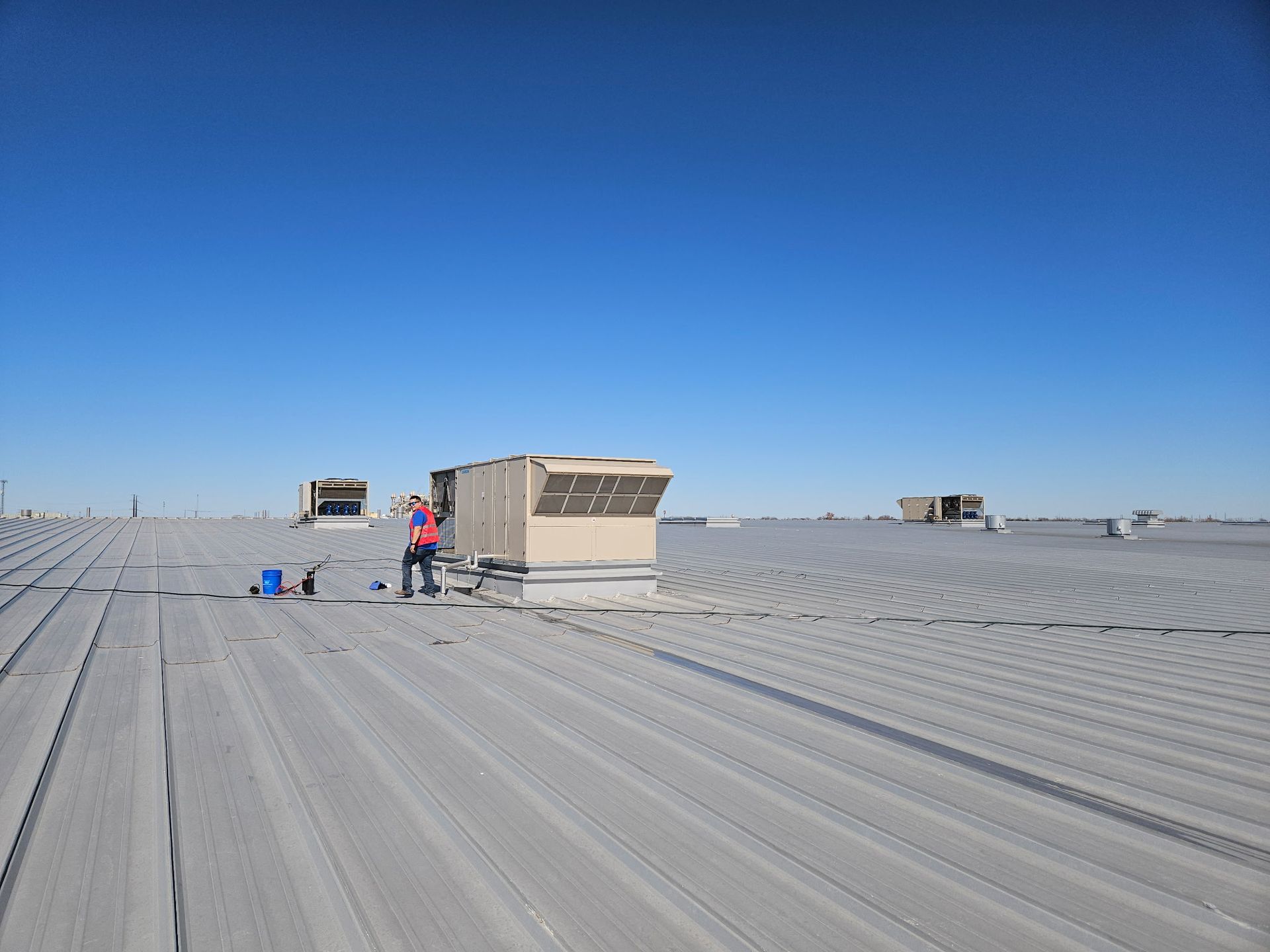 Person working on a rooftop with HVAC units under a clear, blue sky.
