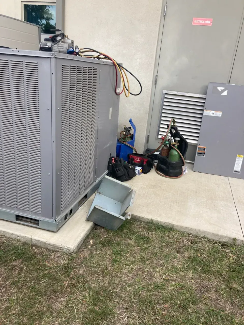 A large air conditioner is sitting on the sidewalk next to a building.