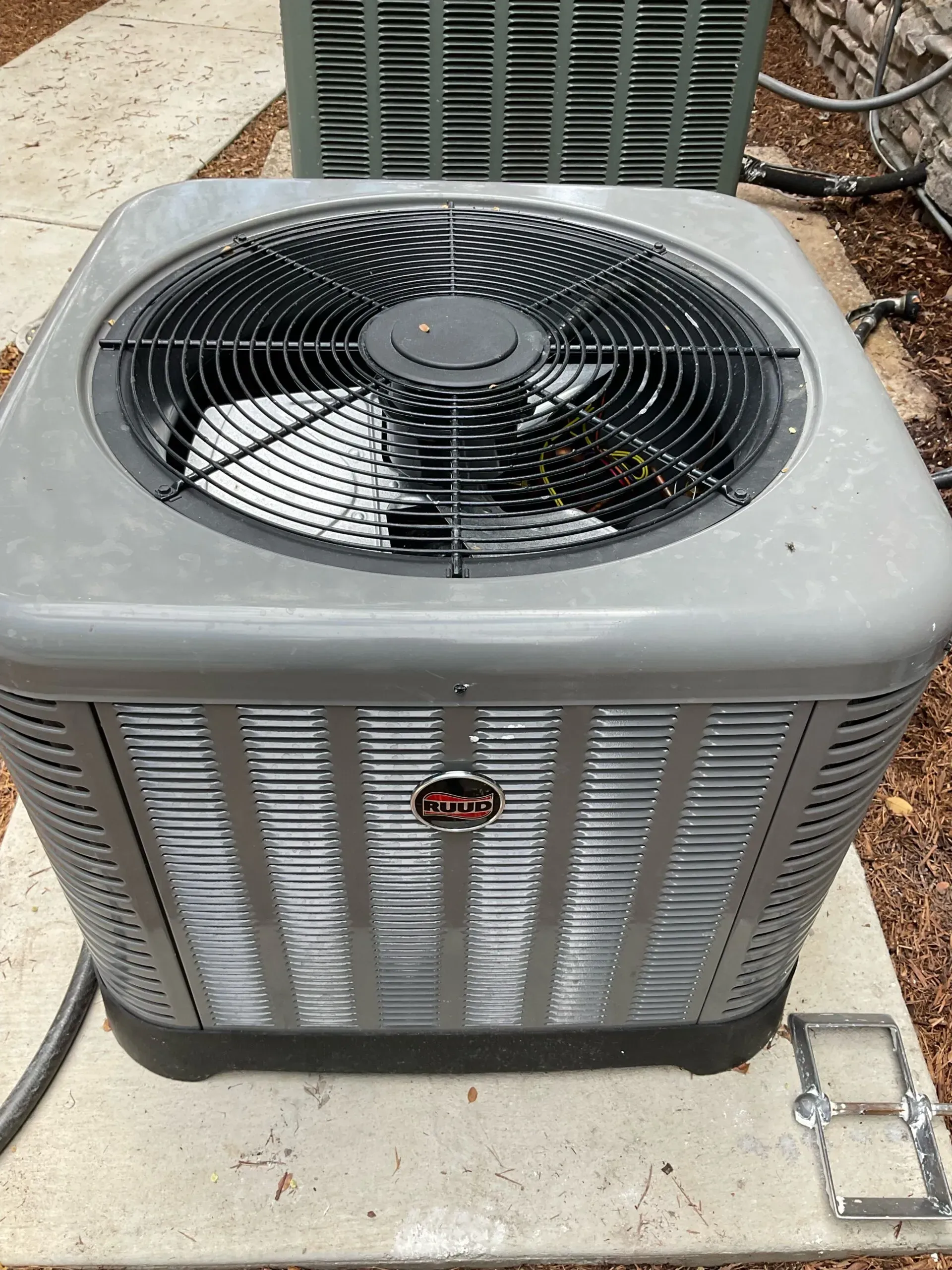 A gray air conditioner is sitting on a sidewalk next to a green air conditioner.