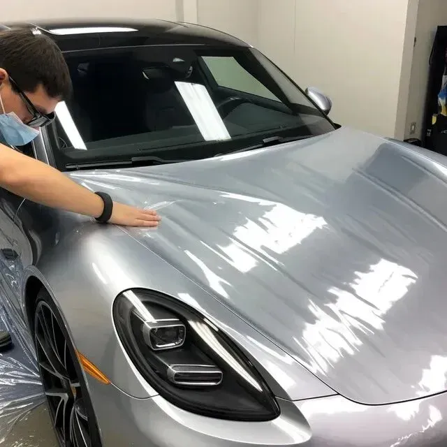 Mobile-Detailing-Man applying clear protective film to a silver Porsche car hood in a garage.