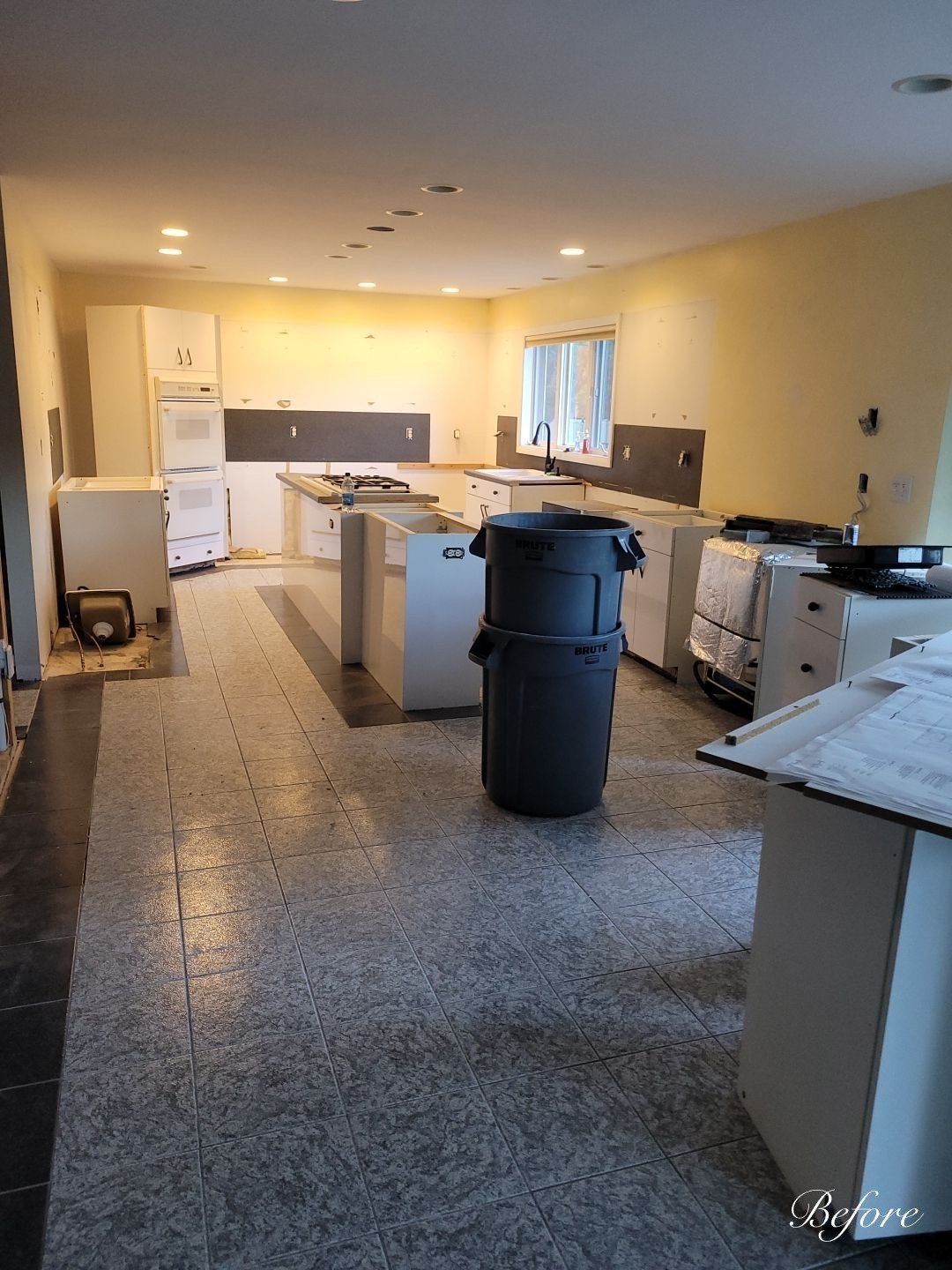 A large kitchen with a trash can in the middle of it.