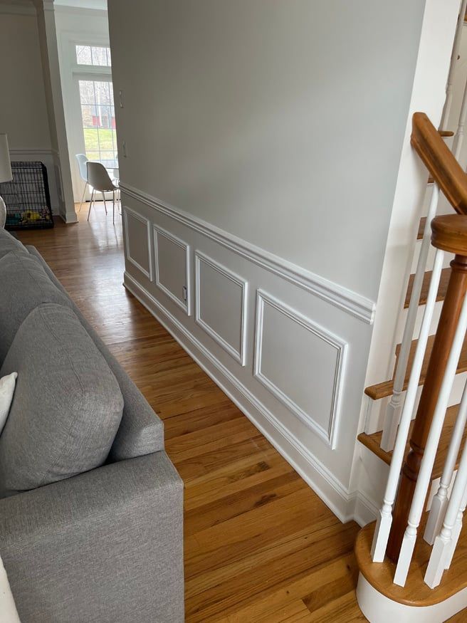 A living room with a couch , stairs and a white railing.