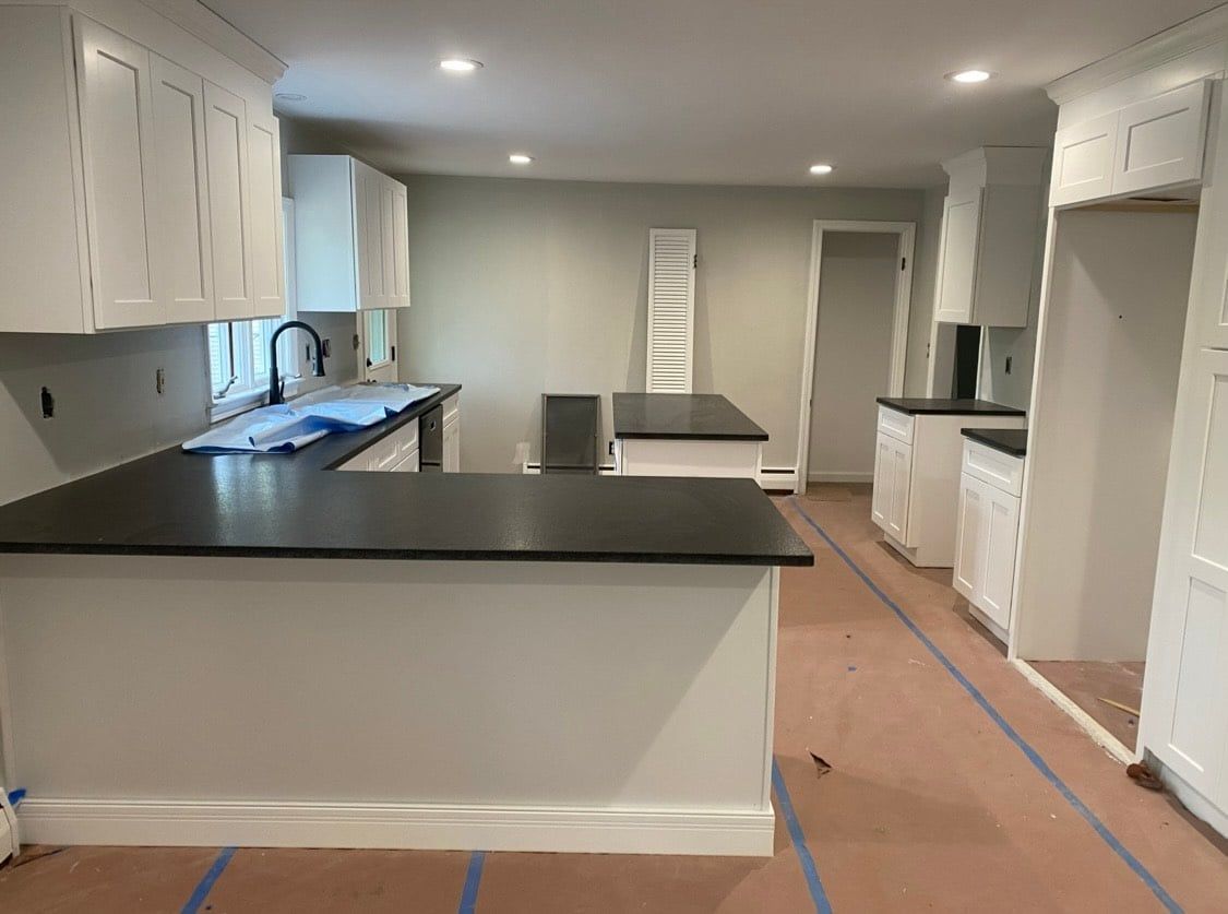 A kitchen with white cabinets and black counter tops is being remodeled.