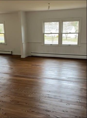 An empty living room with hardwood floors and two windows.