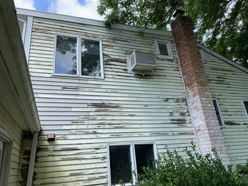 The back of a house with peeling siding and a chimney.