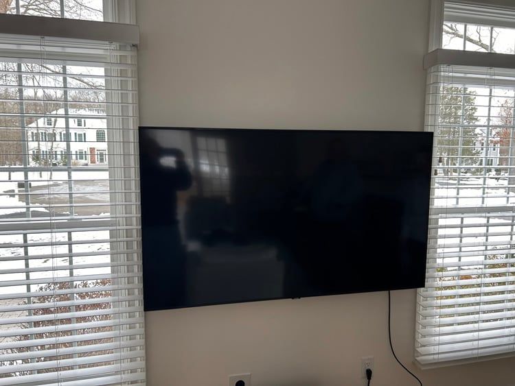 A flat screen tv is mounted on a wall next to two windows.
