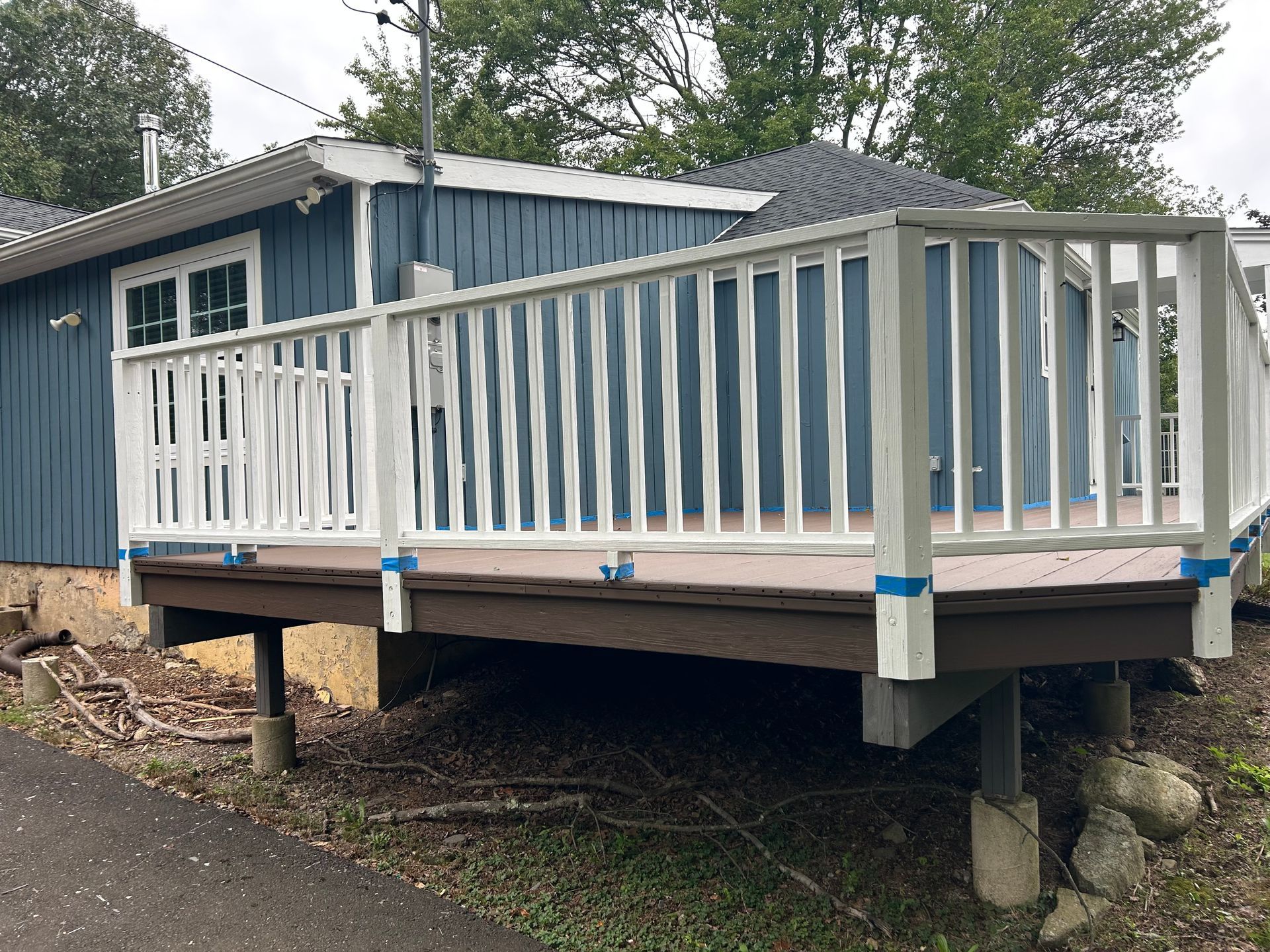 A wooden deck with a white railing is in front of a blue house.