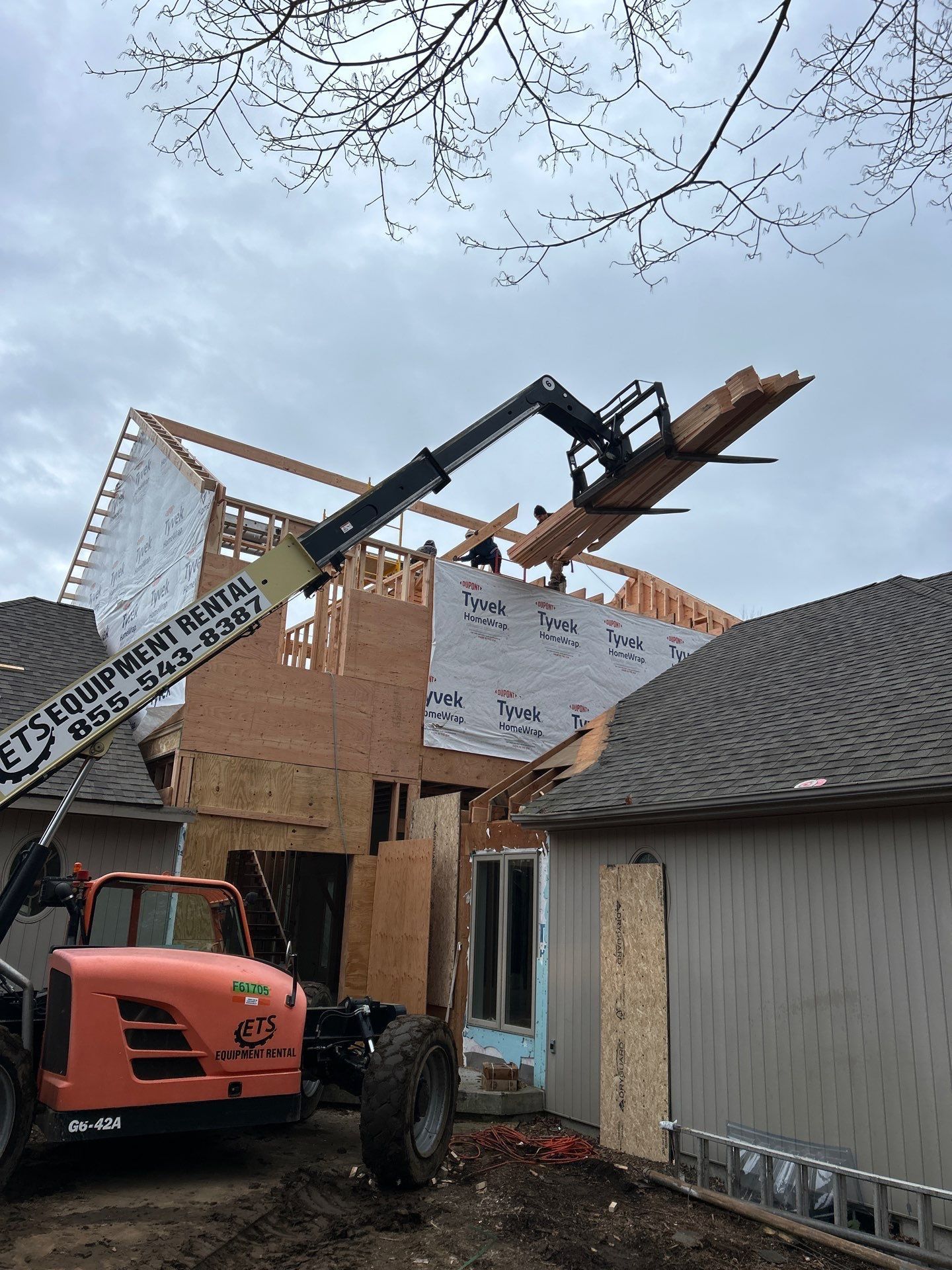 A crane is lifting a piece of wood over a house under construction.