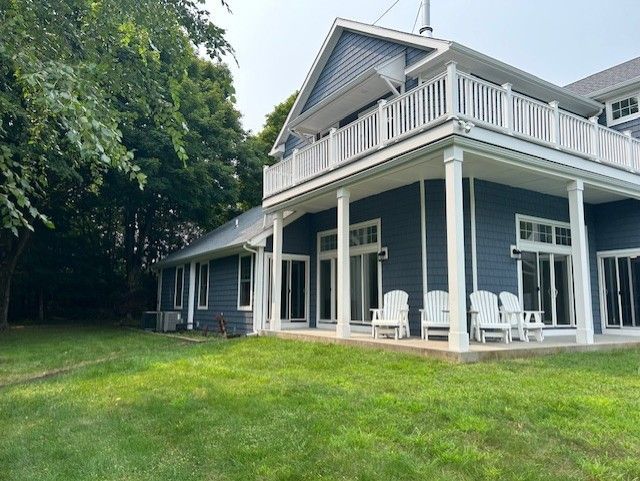 A large blue house with a large porch and chairs in front of it.
