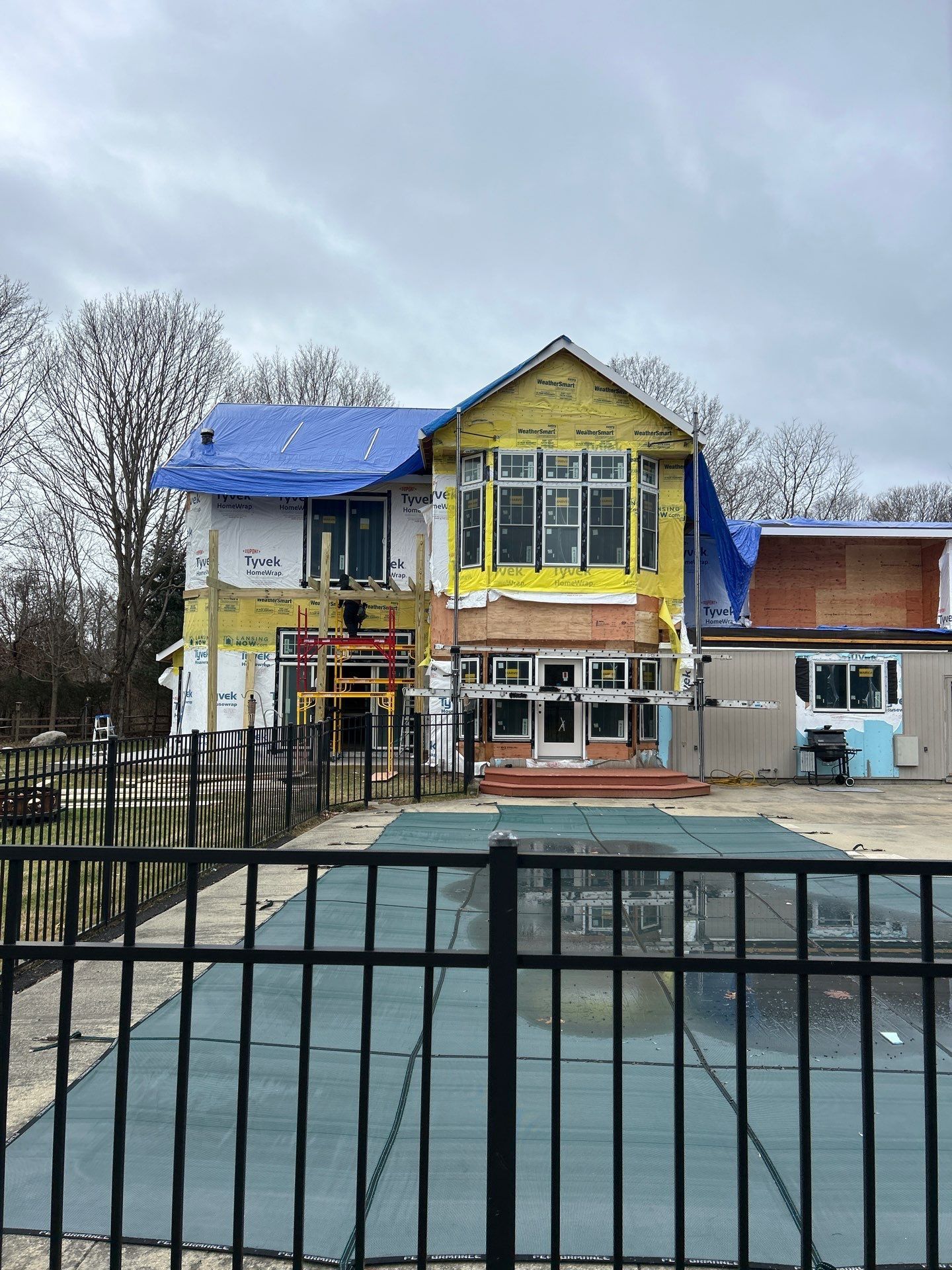 A large house under construction with a pool in front of it.