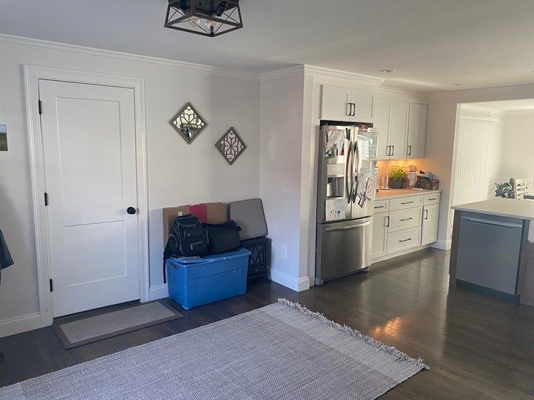 A living room with a blue box on the floor and a stainless steel refrigerator.
