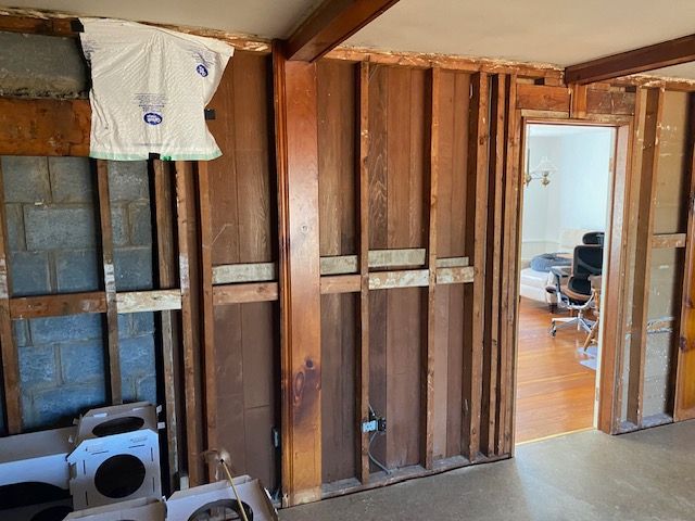 A room with wooden walls and a doorway leading to a bedroom.