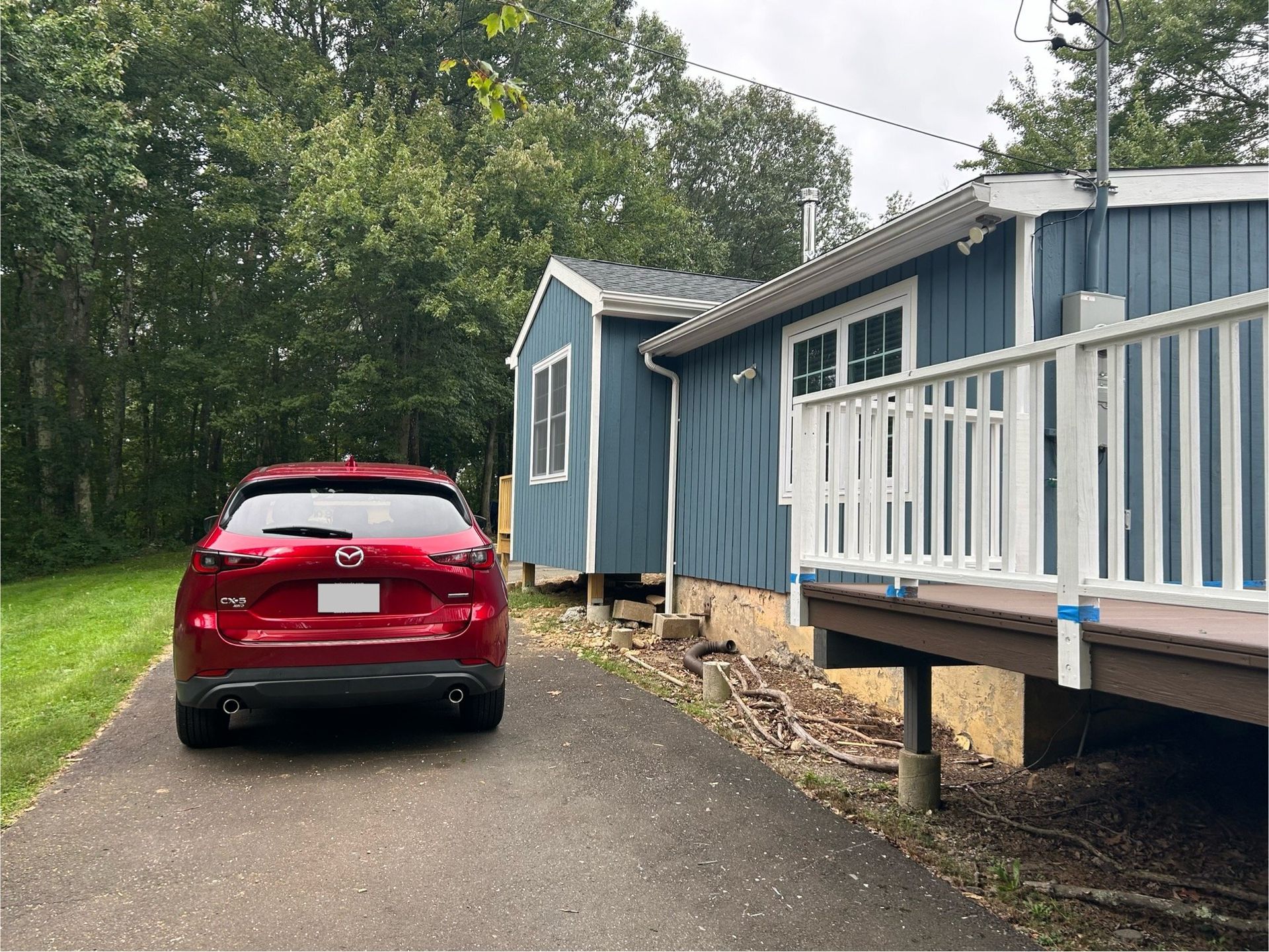 A red car is parked in front of a blue house.