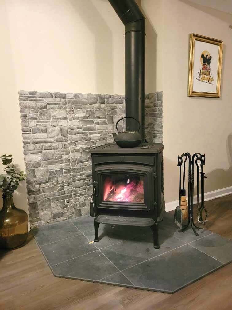 A wood stove is sitting in a living room next to a stone wall.
