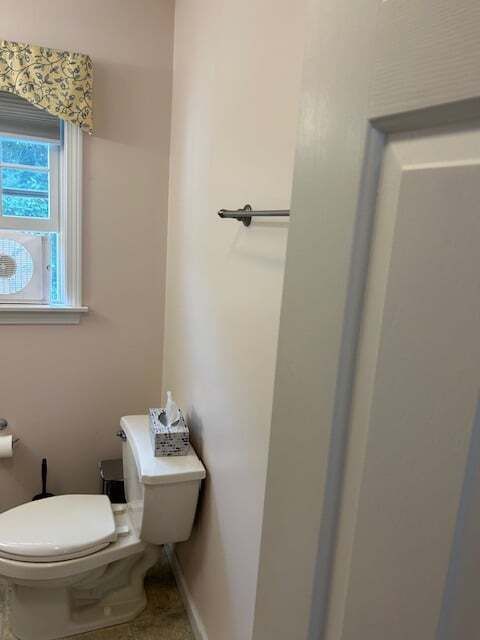 A bathroom with a toilet , tissues , and a window.