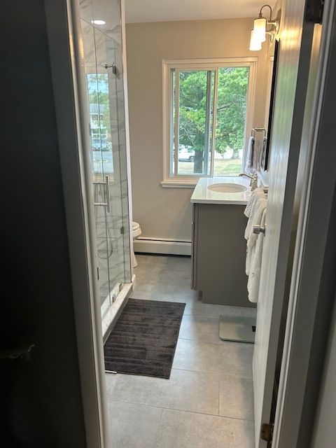 A bathroom with a sink , toilet , shower and window.