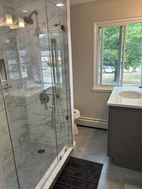 A bathroom with a walk in shower , sink , toilet and window.