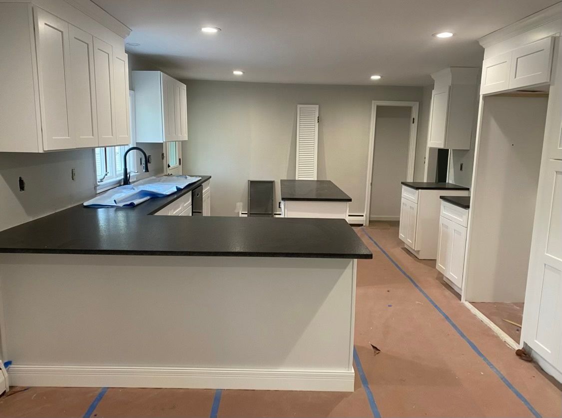 A kitchen with white cabinets and black counter tops is being remodeled.
