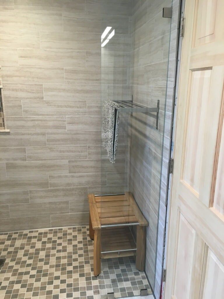 A bathroom with a walk in shower and a wooden bench.
