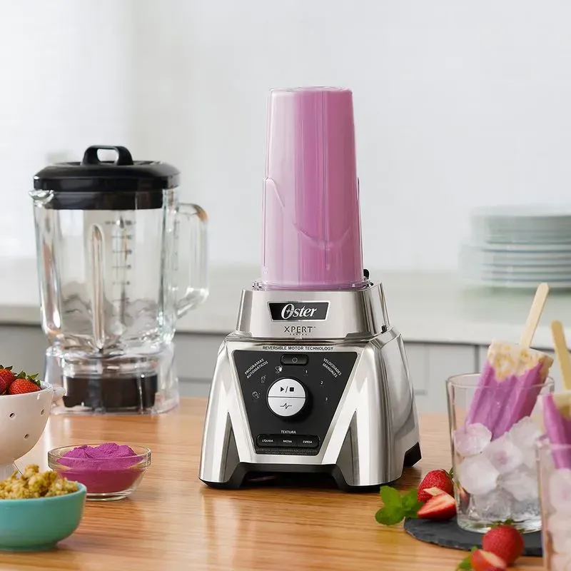 Licuadora con fruta y hielo; un batido en la encimera. Cocina con luz natural.