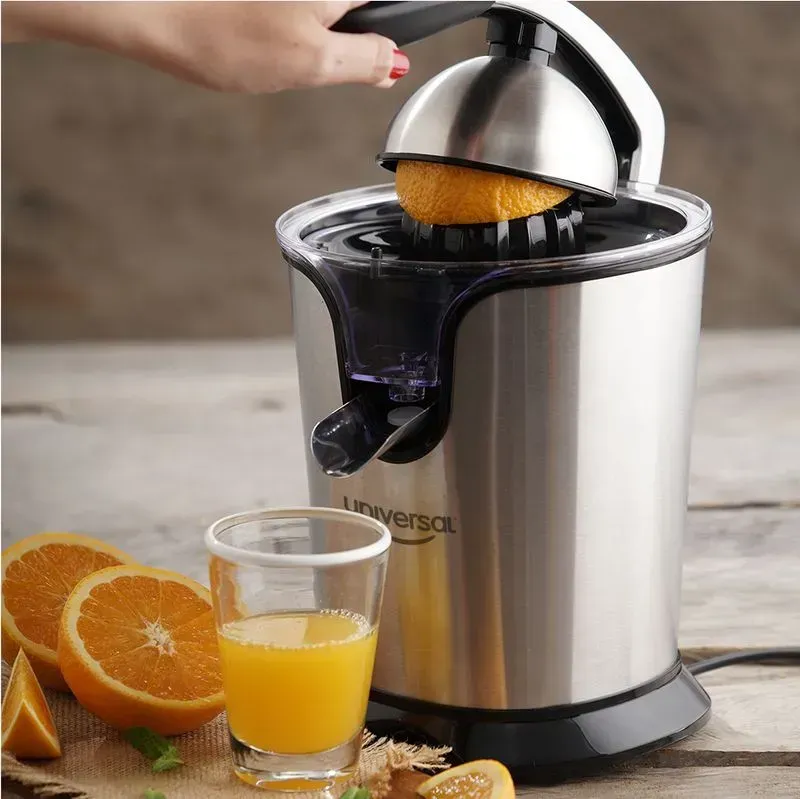 Persona exprimiendo una naranja con un exprimidor eléctrico, junto a un vaso de zumo de naranja y naranjas en rodajas.