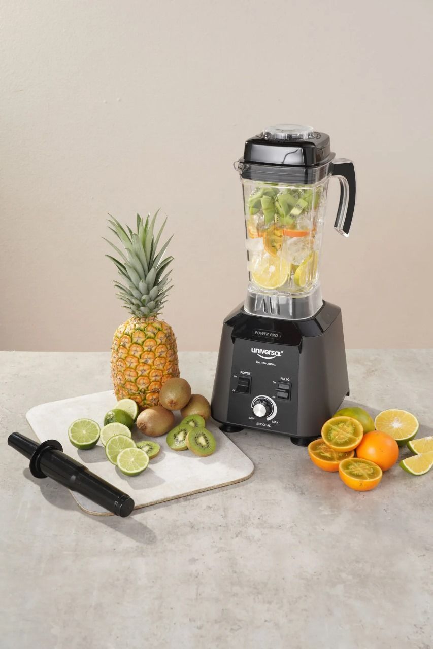 Licuadora con frutas como piña, kiwi, limas y naranjas sobre una encimera clara, lista para un batido.