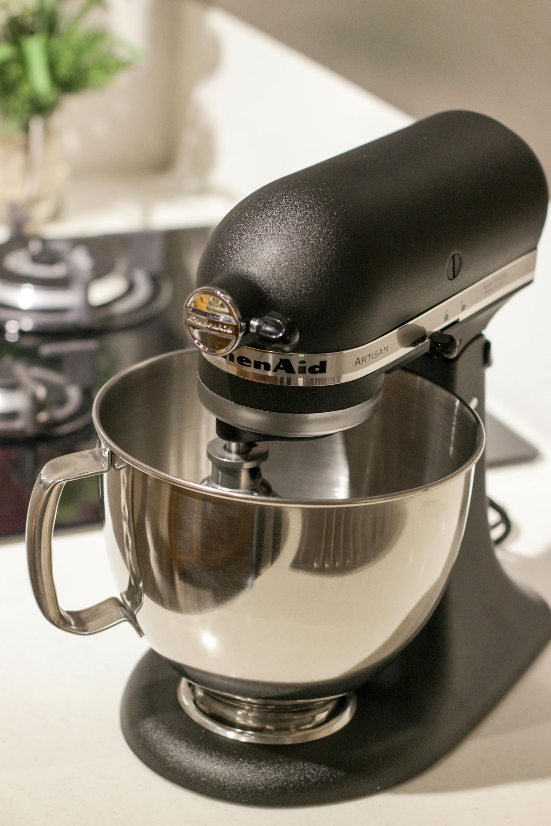 Batidora de pie KitchenAid negra con recipiente plateado, sobre una encimera blanca.