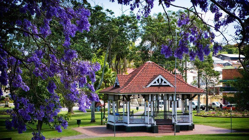 A gazebo in a park surrounded by trees and purple flowers.