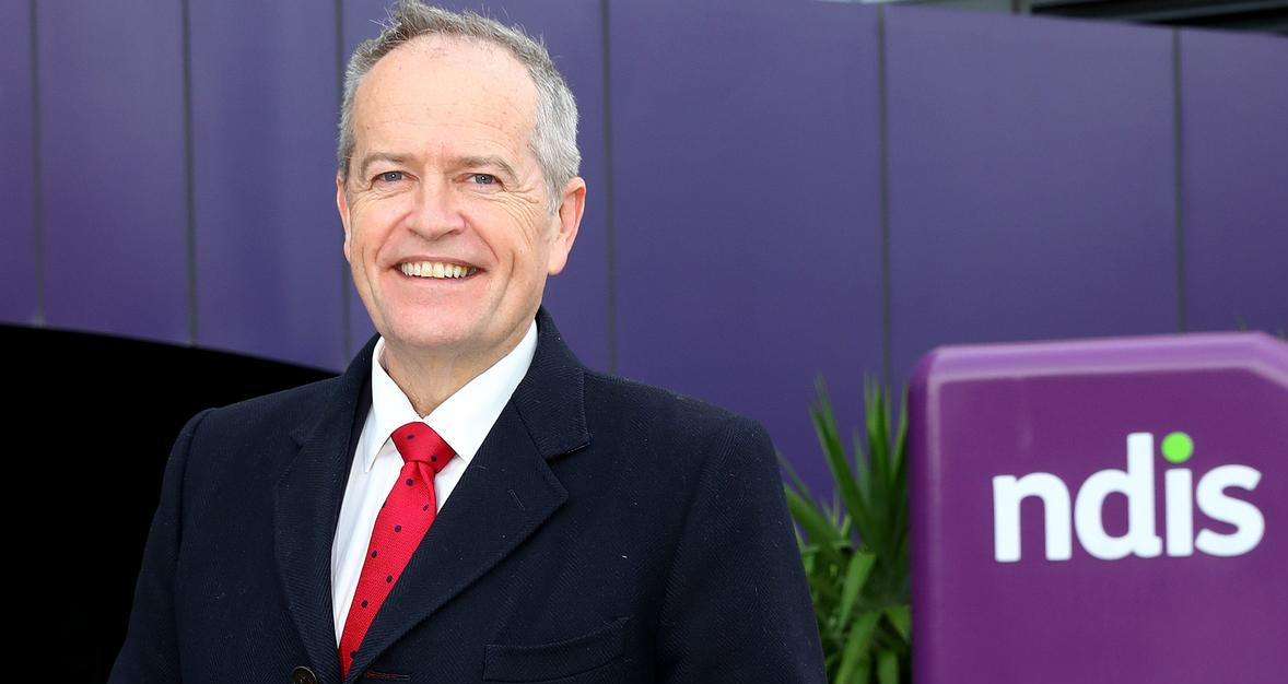A man in a suit and tie is smiling in front of a purple building.