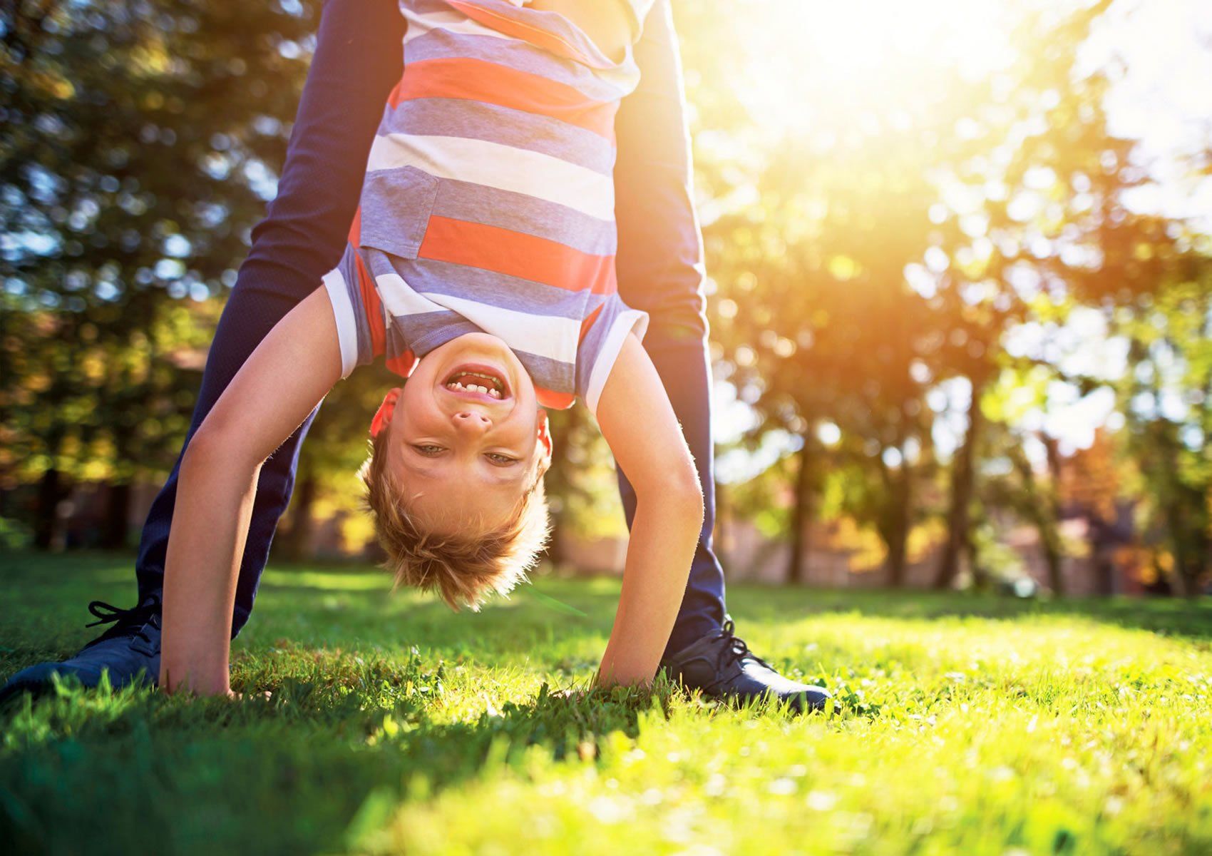 A young boy is doing a handstand in the grass in a park.