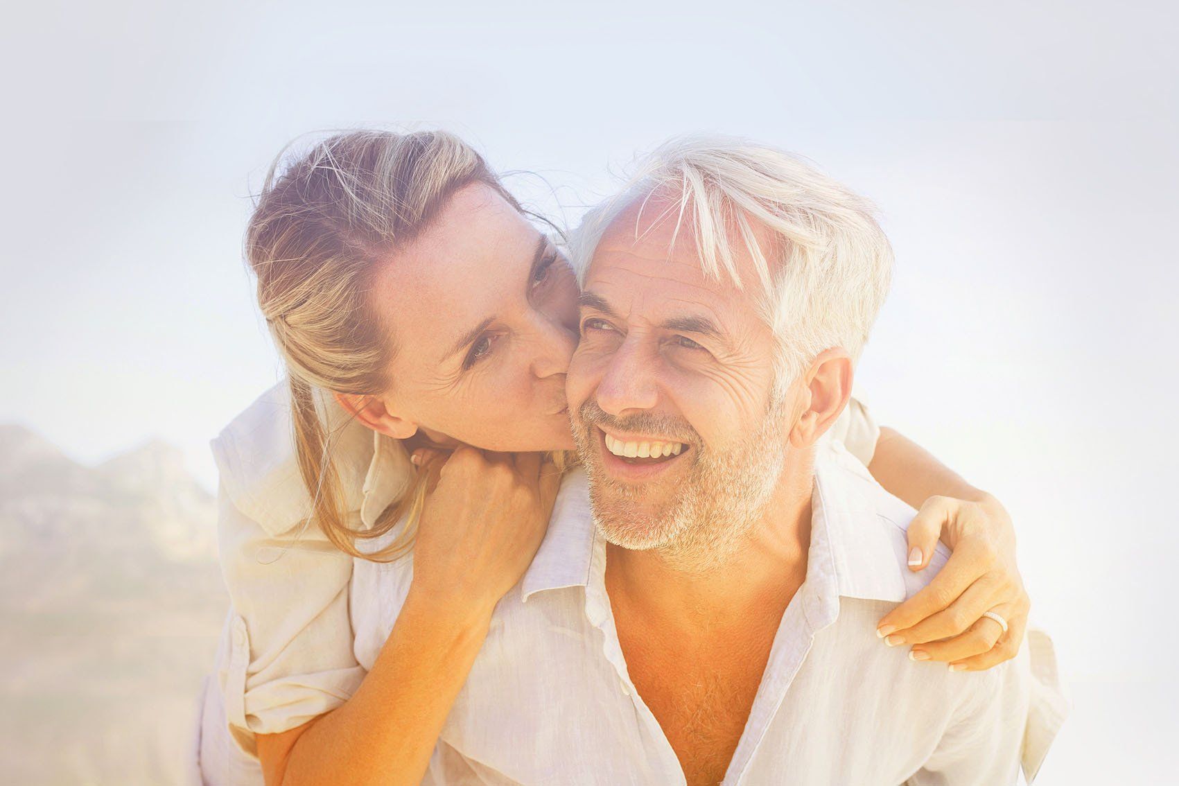 A woman is kissing a man on the cheek on the beach.