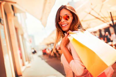 A woman is holding shopping bags and smiling while walking down the street.