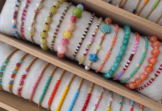 Armbanden met kleurrijke kralen, uitgestald op een crèmekleurig kussen in een houten opbergdoos.