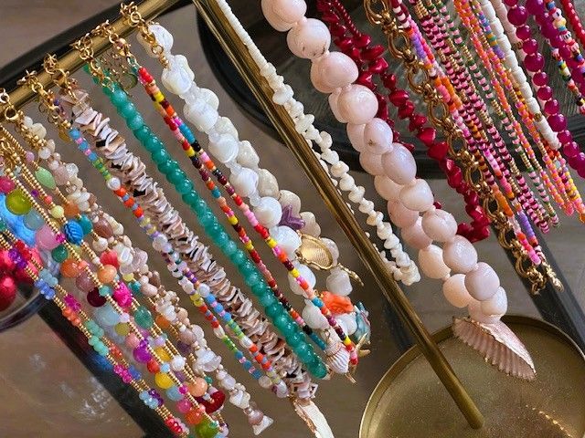 Kralenkettingen in diverse kleuren en designs, tentoongesteld op een gouden standaard.