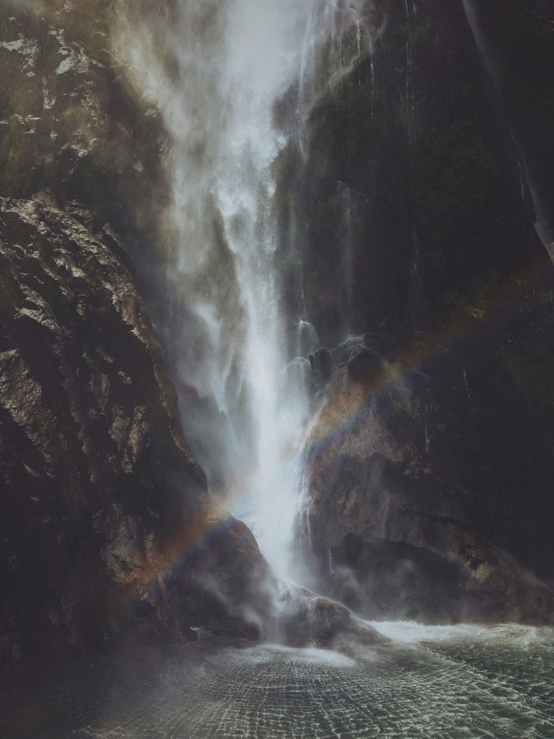 A waterfall is coming down a rocky cliff into a body of water.