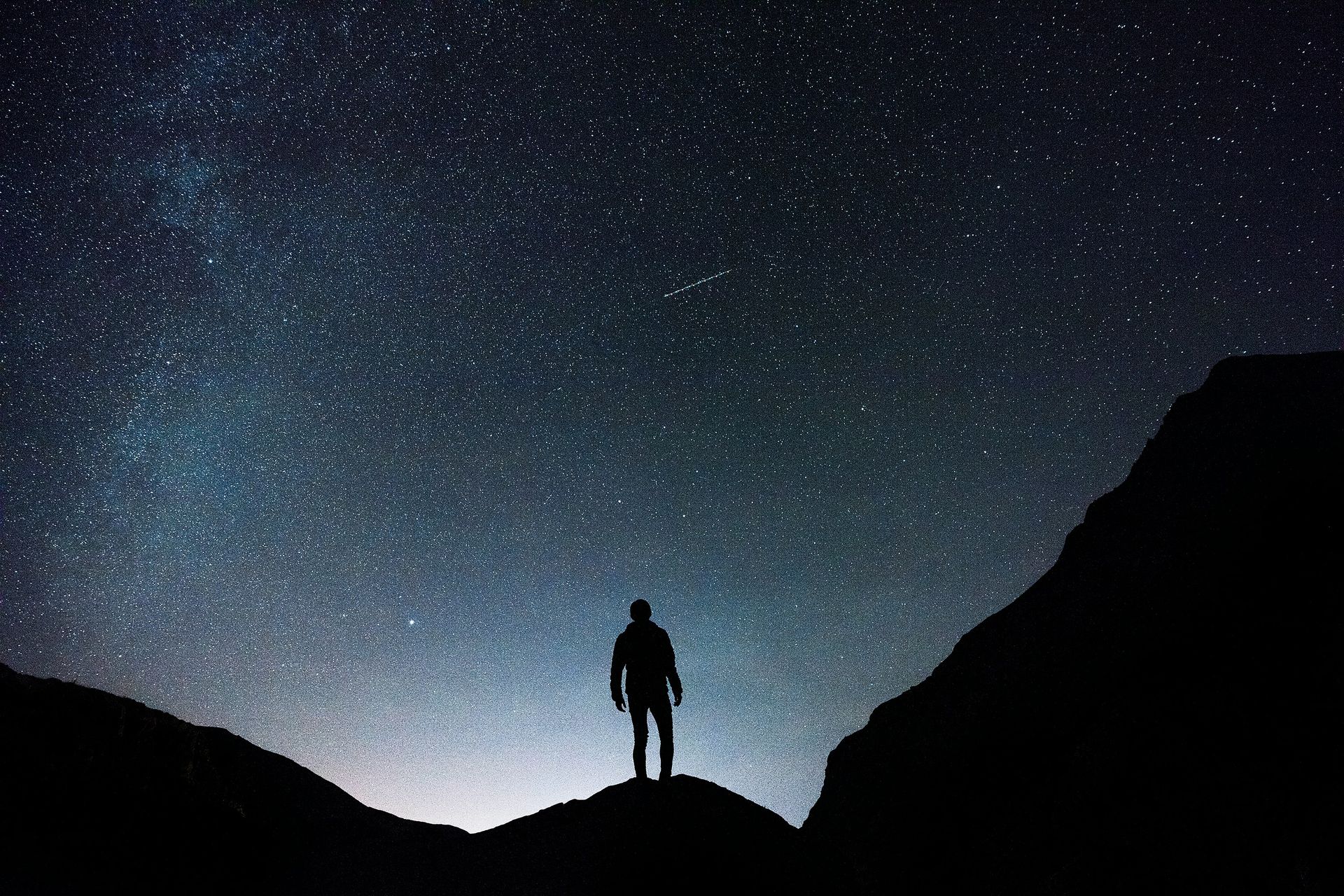 A man is standing on top of a mountain under a starry night sky.
