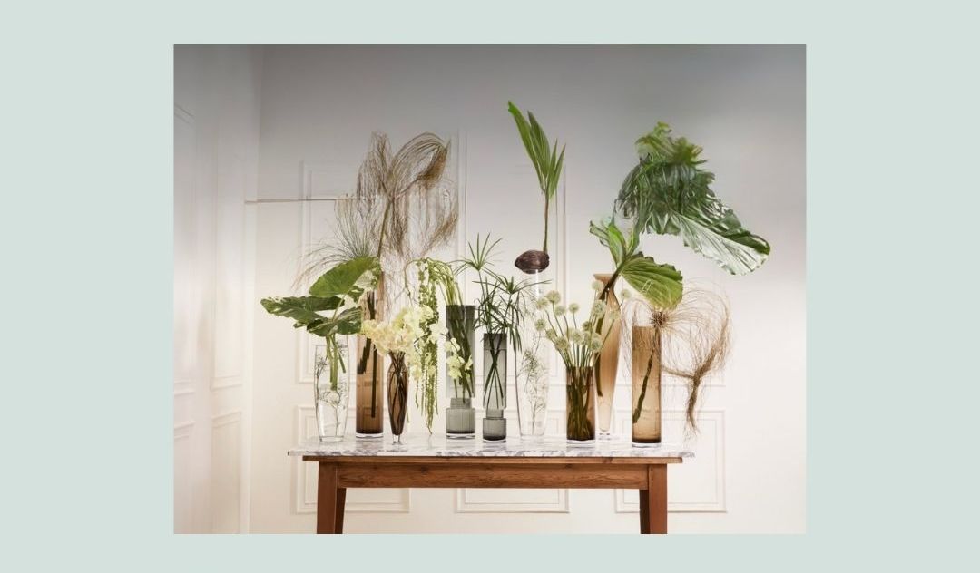 a wooden surface with glass vessels holding plants and flowers