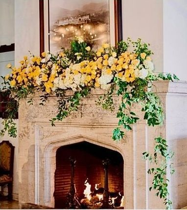 a fireplace with beautiful yellow, cream flowers and greenery
