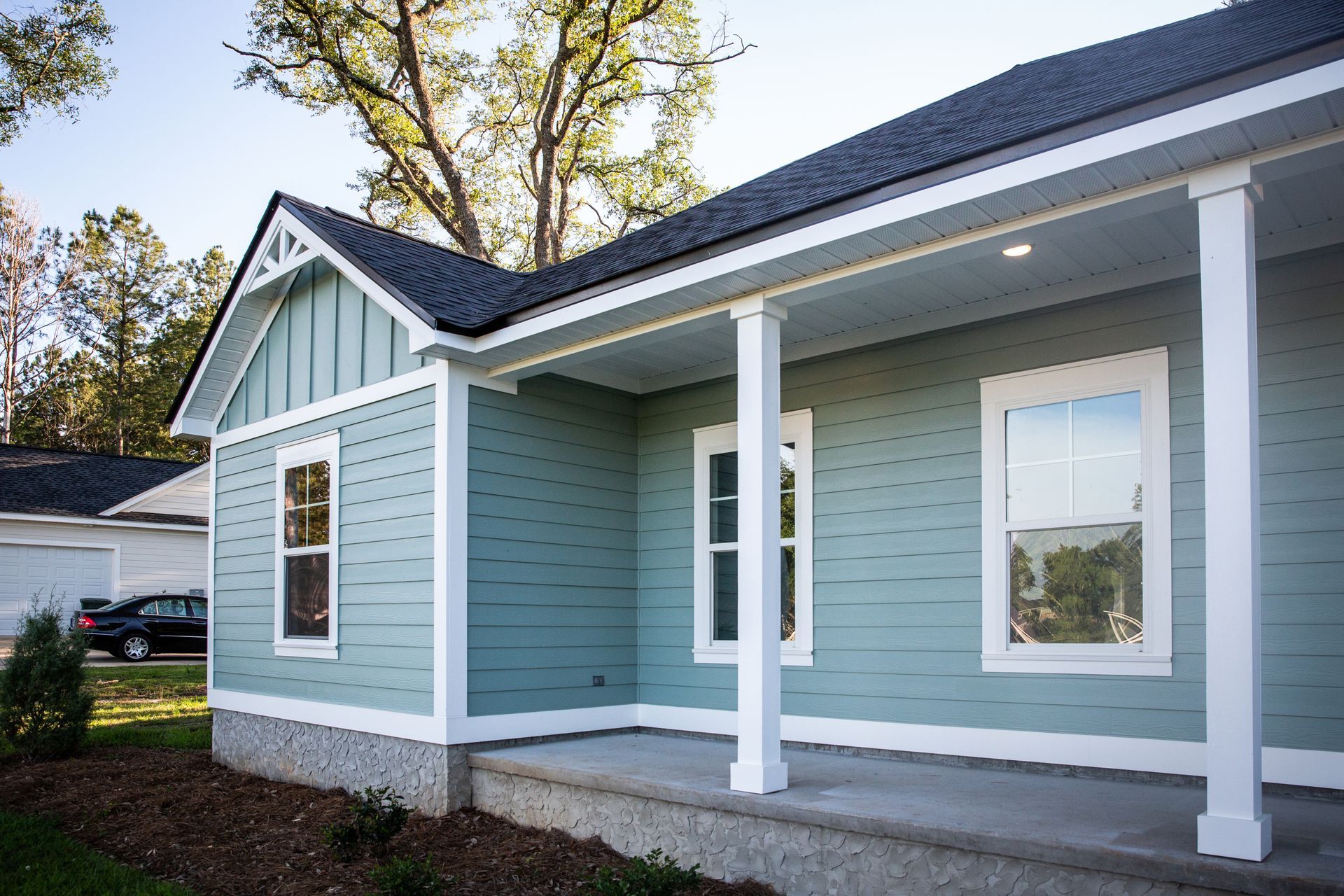 Blue house with white trim, porch, and windows, next to trees and grass.