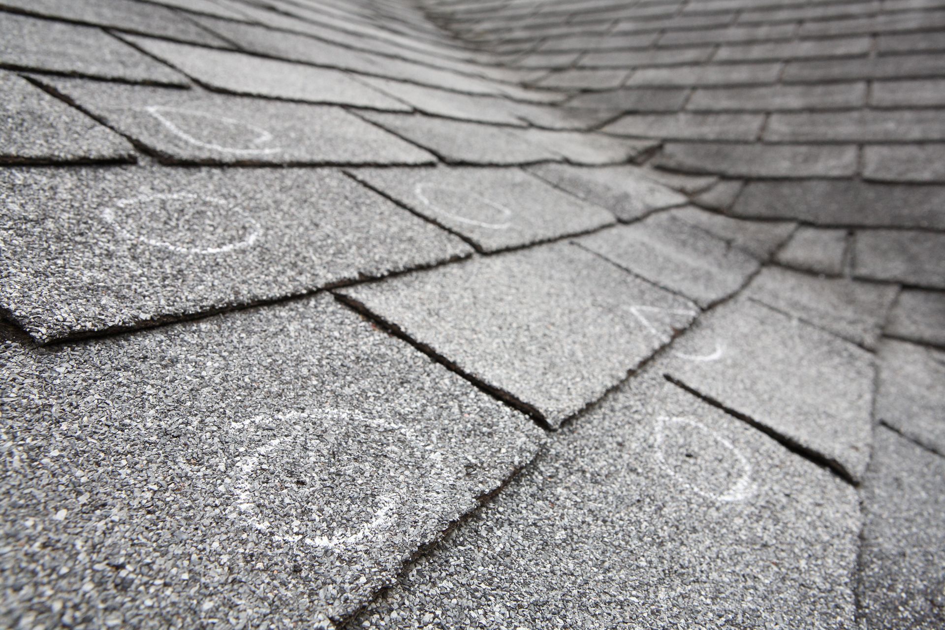 Damaged gray asphalt roof shingles with chalk circles marking hail damage.