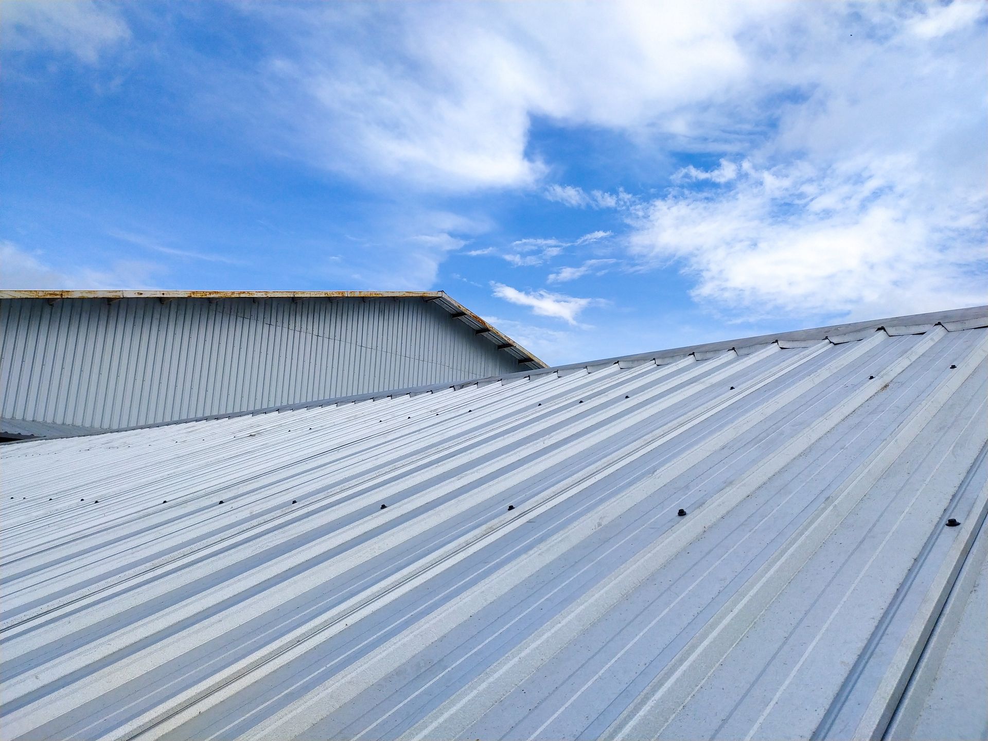 Metal roof with ridges against a blue sky with clouds.