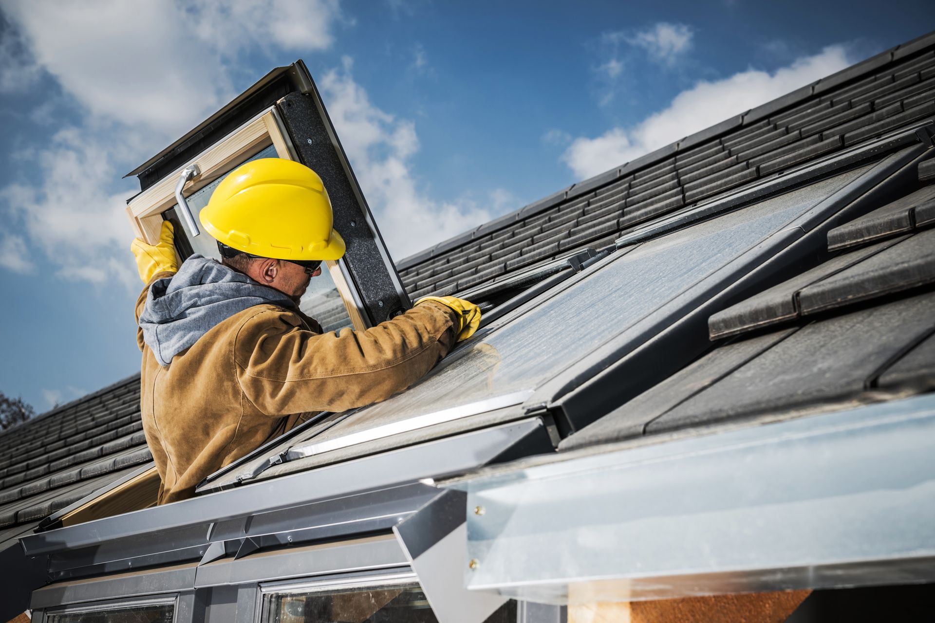 Construction worker in yellow hard hat installing solar panel on a roof.
