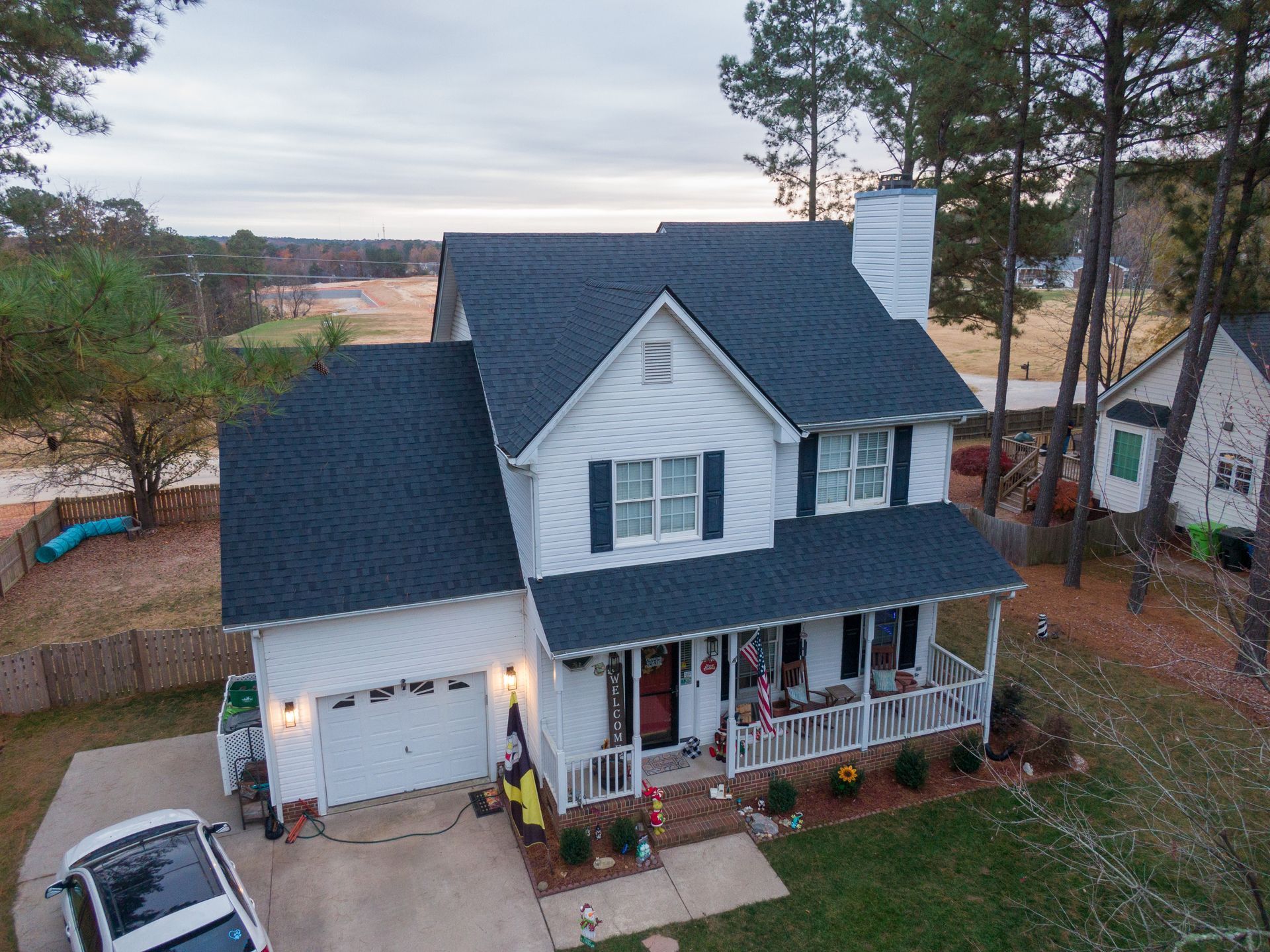 White two-story house with black roof, covered porch, and attached garage; car parked in driveway.