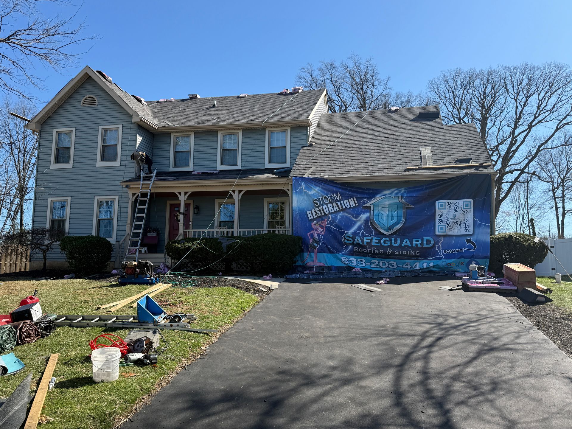 House with a damaged roof being repaired; a large banner covers part of the building.