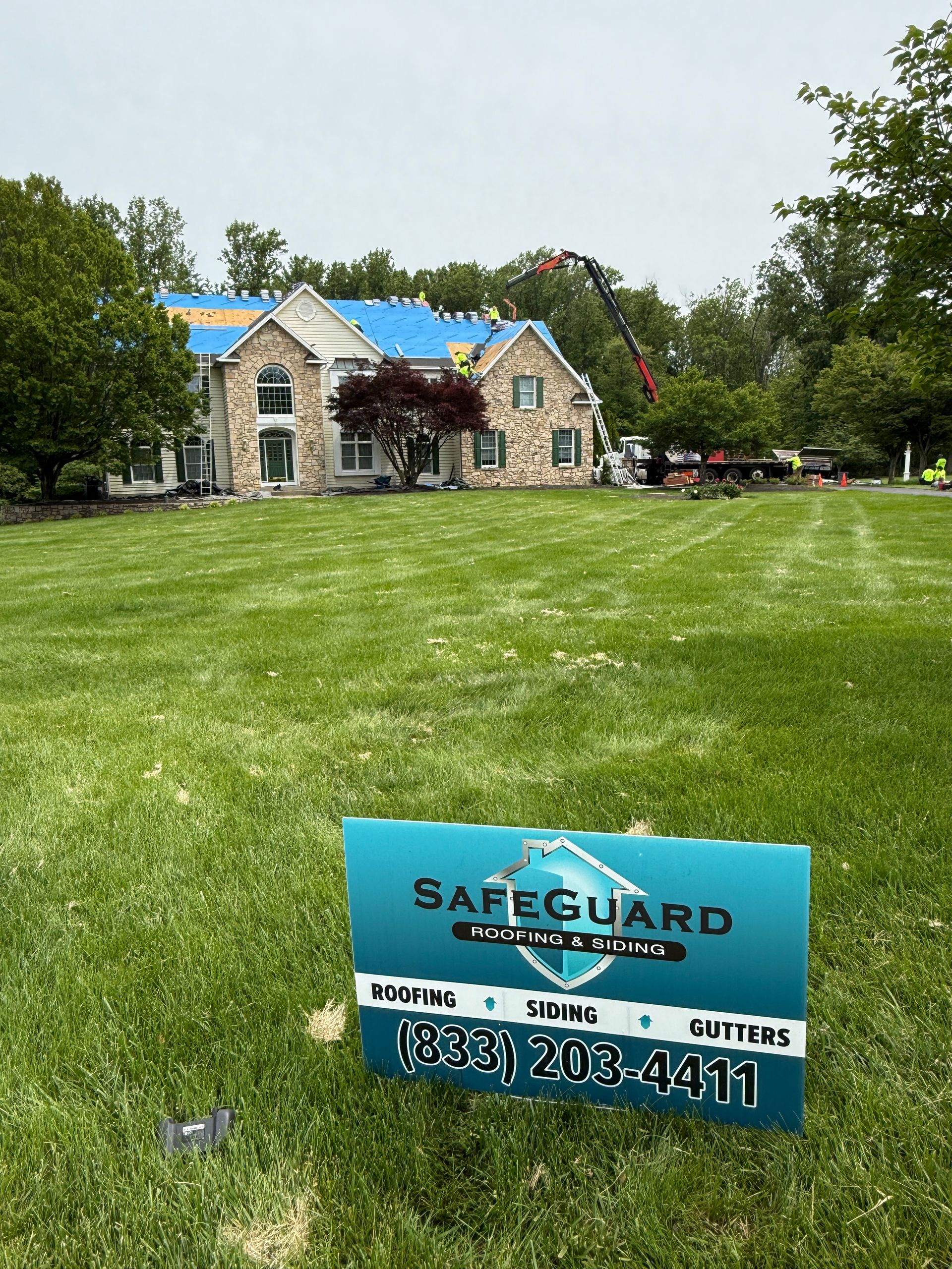 Safeguard Roofing sign in front of a house with roof replacement in progress on a green lawn.
