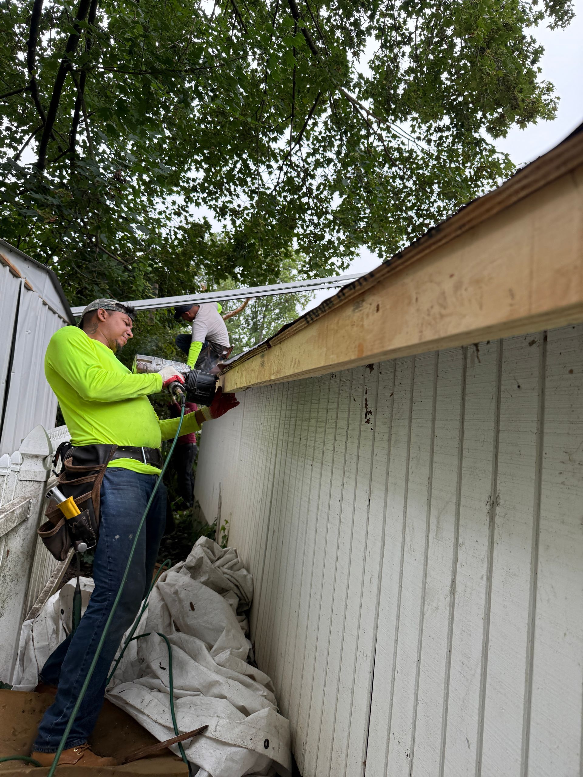 Two construction workers installing new roofing on a white building, one using a nail gun.